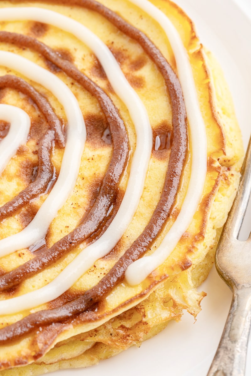 Close up of keto cinnamon roll pancakes on a white plate with a silver fork.