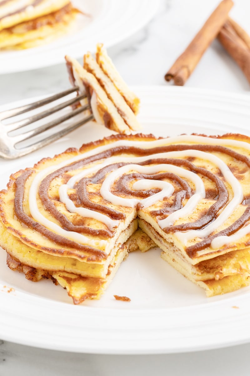 Three keto cinnamon roll pancakes on a white plate with a bite cut out on a silver fork.
