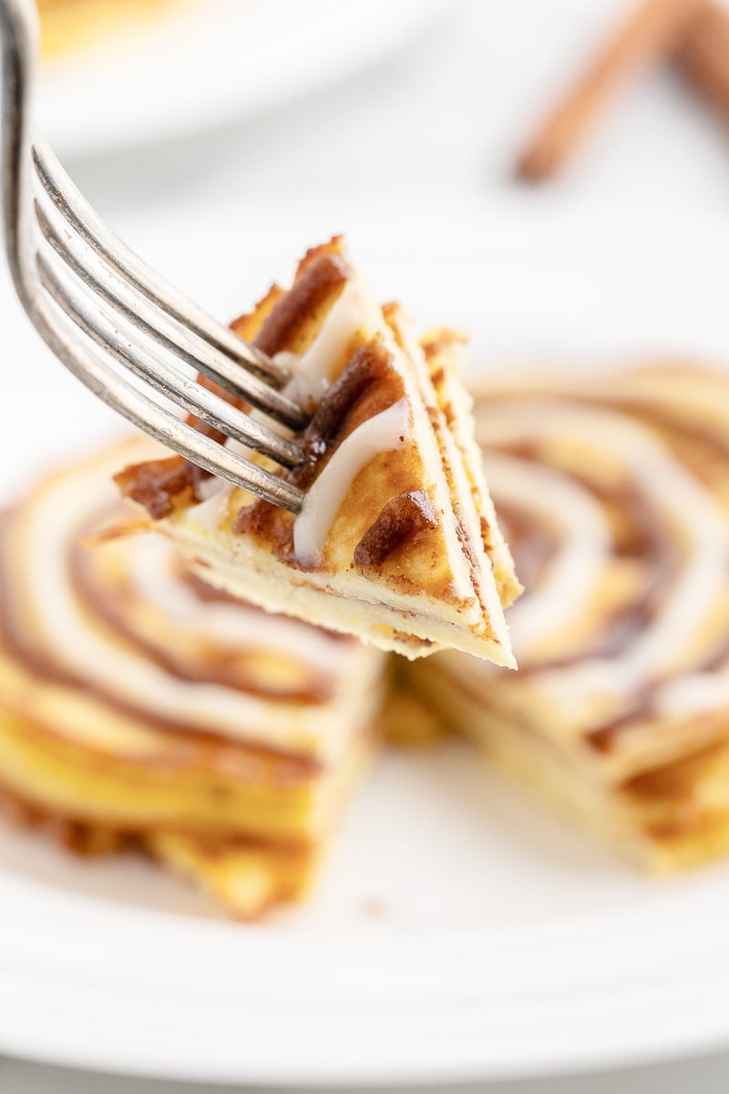 Keto cinnamon roll pancakes on a white plate with a silver fork holding a bite closer to the camera.