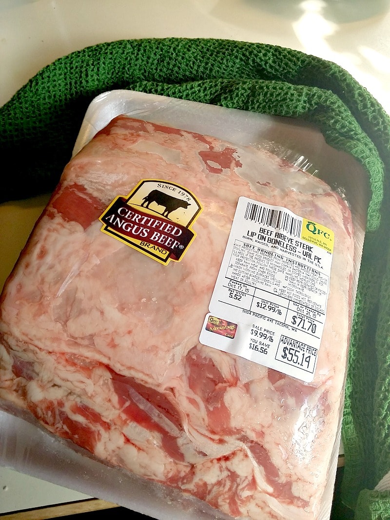 Boneless beef rib roast in the package on a kitchen counter with a green hand towel behind it.
