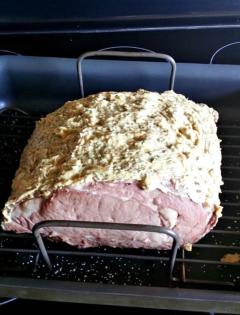 Boneless rib roast covered in roasted garlic, dijon mustard, and fresh herbs in a roasting pan.