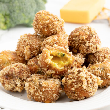 Keto broccoli cheese balls piled on a white plate with a head of broccoli and block of cheese in the background.