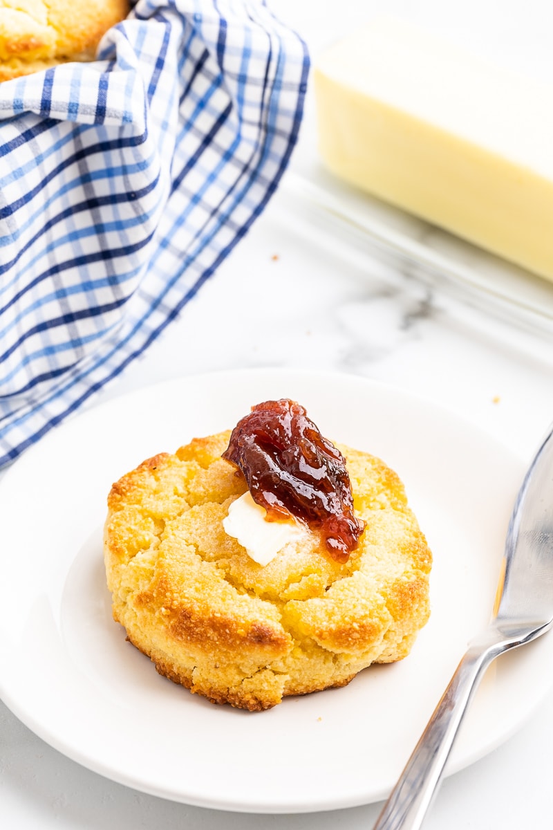 Keto buttermilk biscuit on a white plate with butter and jam on top of it.