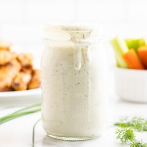 Homemade ranch dressing in a mason jar on a white counter with chicken wings and veggies in the background.