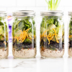 Four mason jars full of low carb taco salad on a white marble counter.