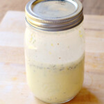 Creamy low carb lemon vinaigrette in a mason jar on a wooden cutting board.
