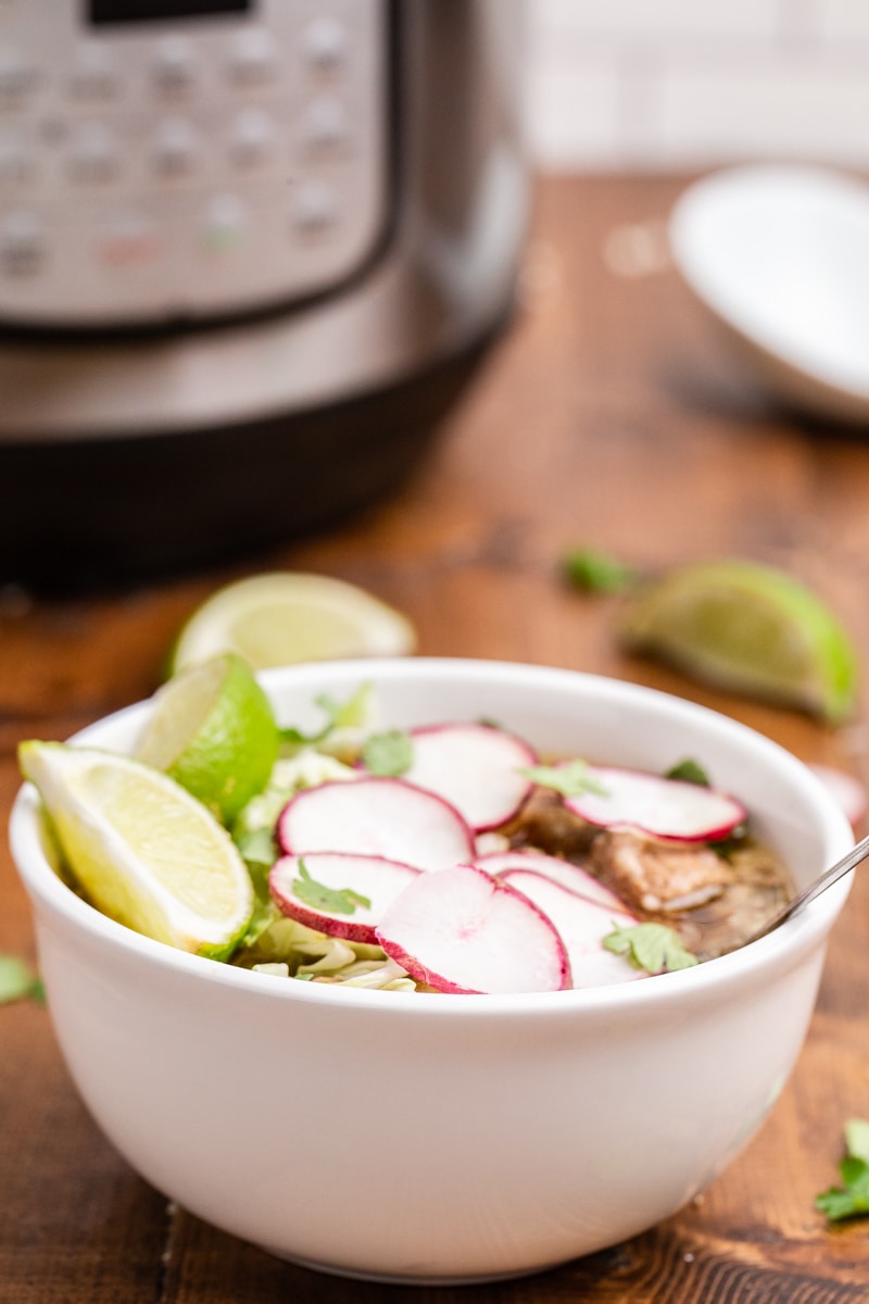 Keto Pork Pozole Verde in a white bowl topped with thin sliced radish, cilantro leaves, and lime wedge.