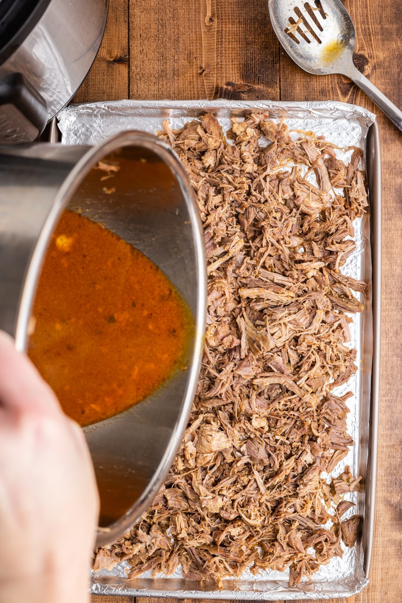 A baking sheet with the shredded carnitas on it 1/3rd of the sauce being poured over the top, step 9.