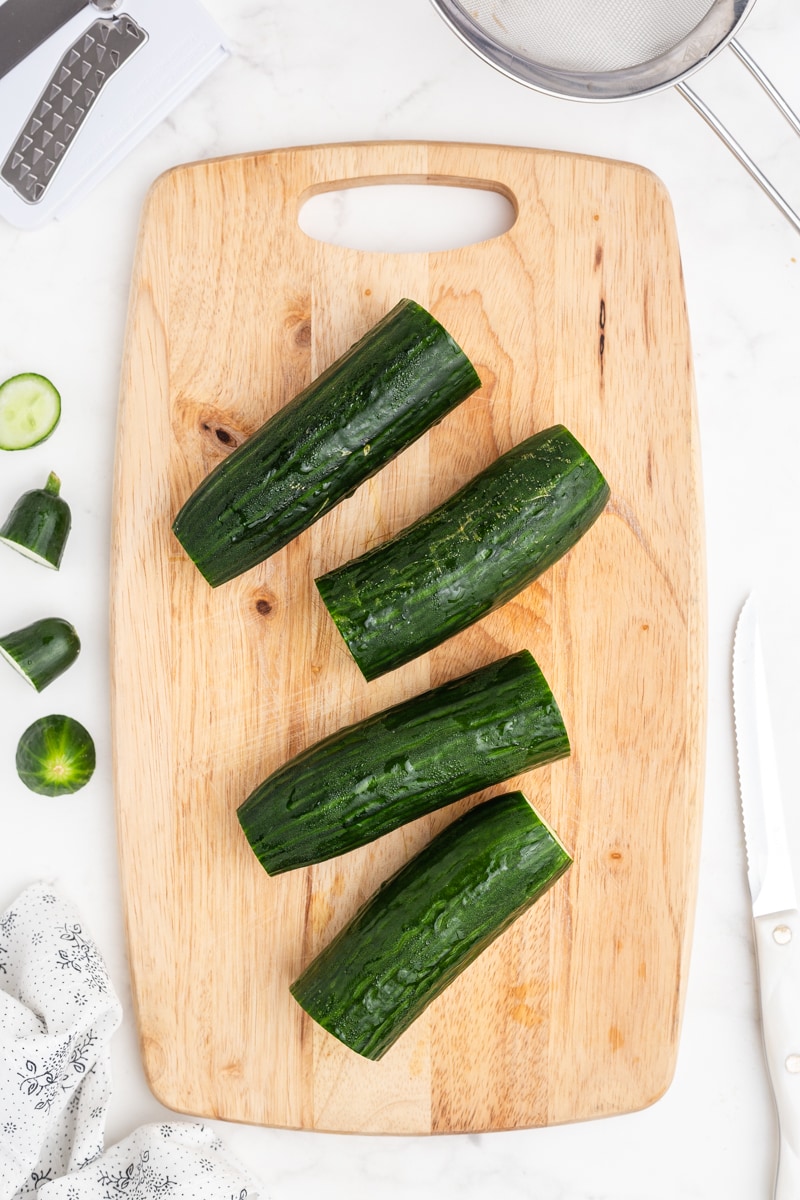 English cucumbers with the ends cut off and cut in half on a wooden cutting board, step 1.