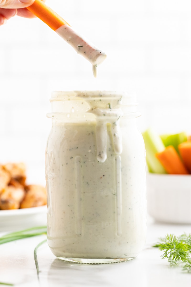 Someone dipping a carrot stick into homemade keto ranch dressing.