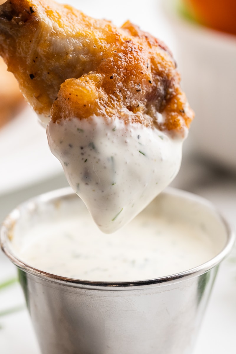 A chicken wing being dipped into homemade ranch dressing.