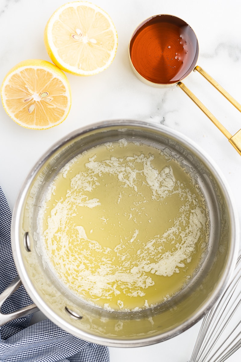Butter melting in a saucepan with a lemon and a spoonful of honey next to the pot.