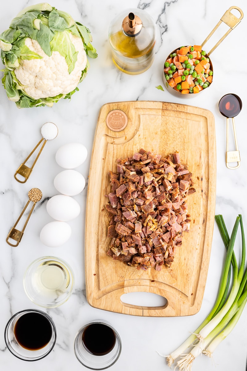 overhead view of the ingredients needed to make Ham Fried Cauliflower Rice on a white marble counter.
