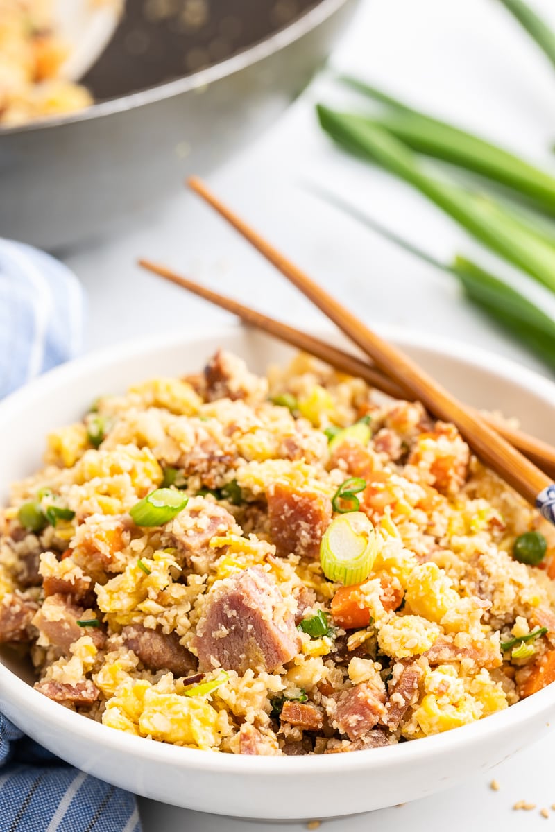 Ham fried cauliflower rice in a white bowl with wooden chops sticks.