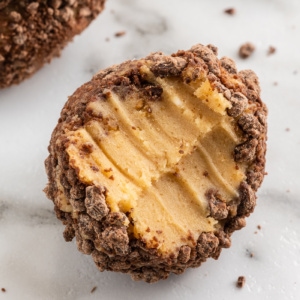 A chocolate peanut butter cheesecake fat bomb with a bite taken out of it on a white marble counter.