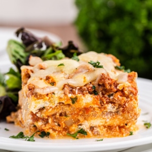 A serving of keto lasagna on a white plate with a side salad.