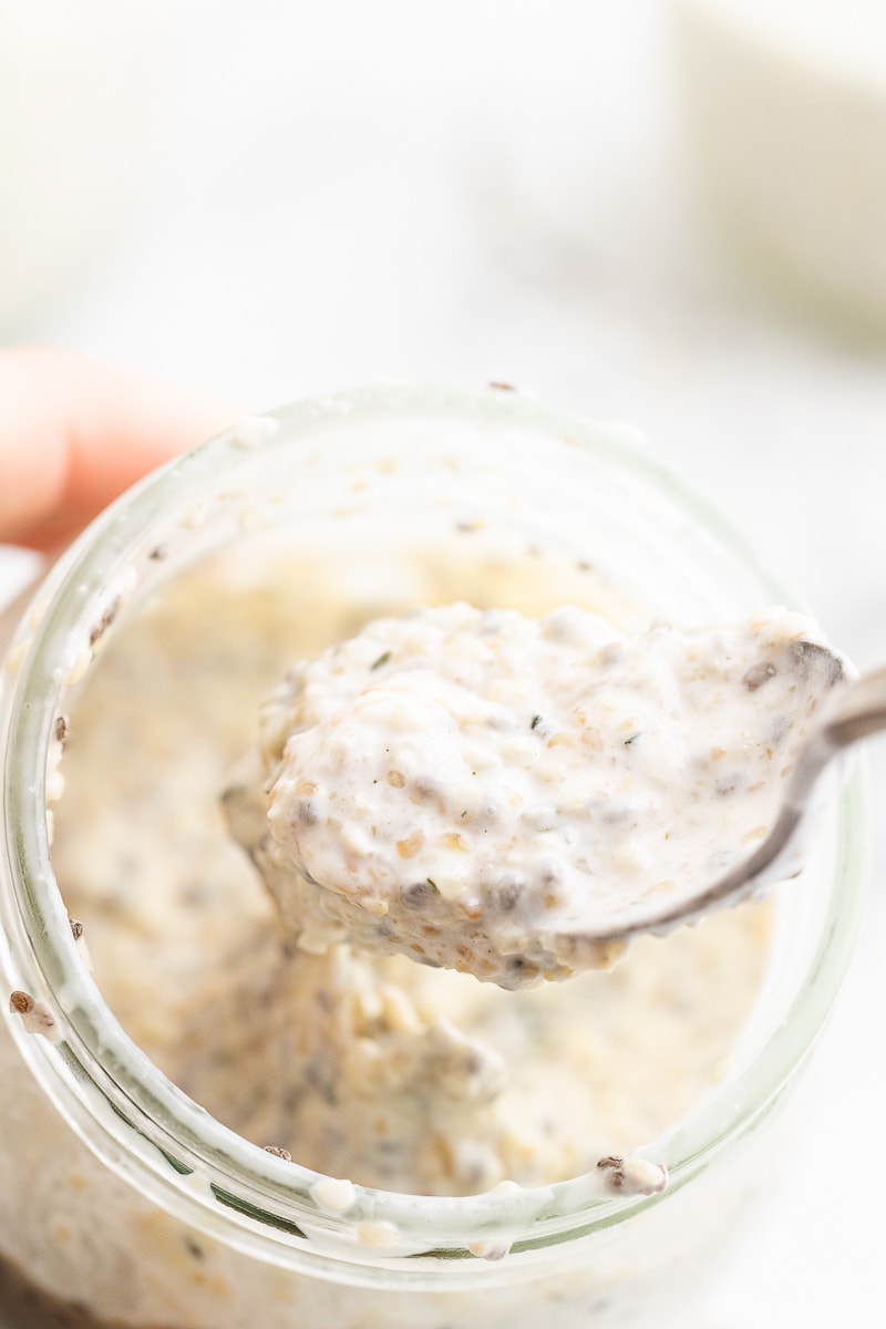 A close-up photo of keto oatmeal in a small mason jar. The oatmeal has thickened and has a creamy texture. A silver spoon is scooping out a small portion from the top of the oatmeal.