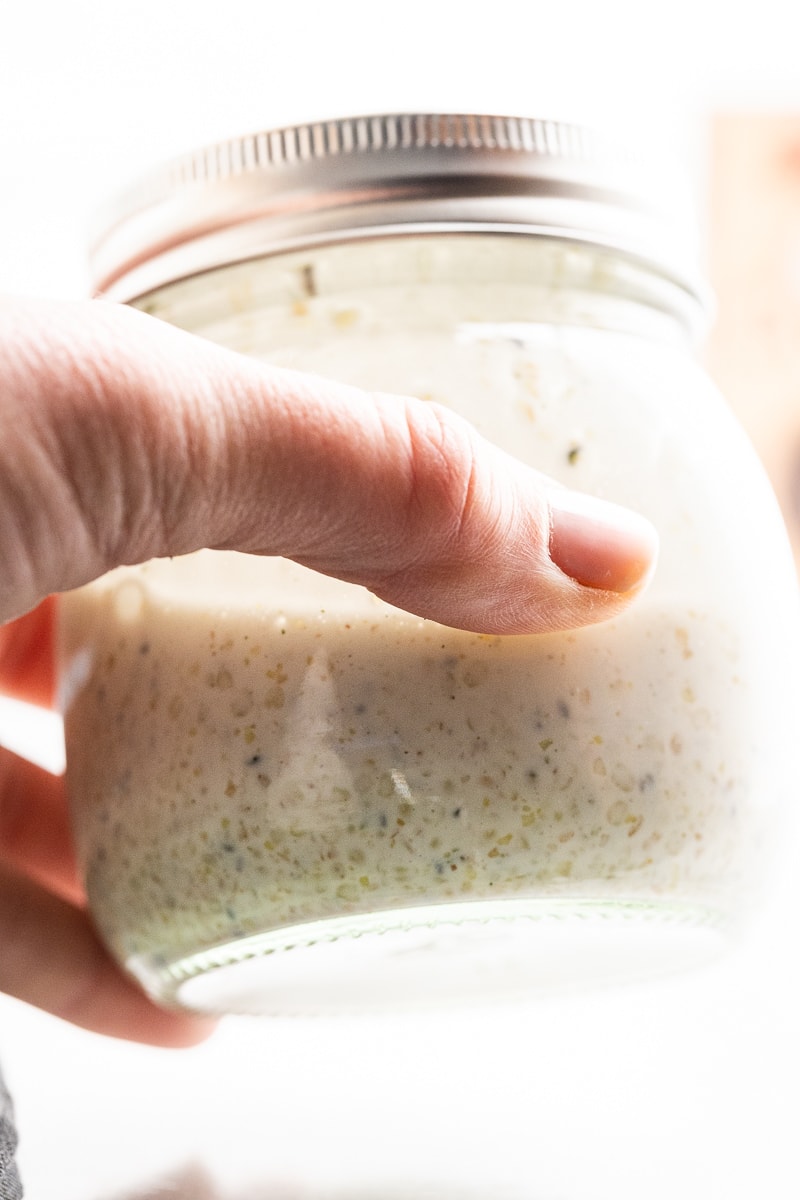 A white male presenting hand shaking a small mason jar filled with keto oatmeal ingredients.