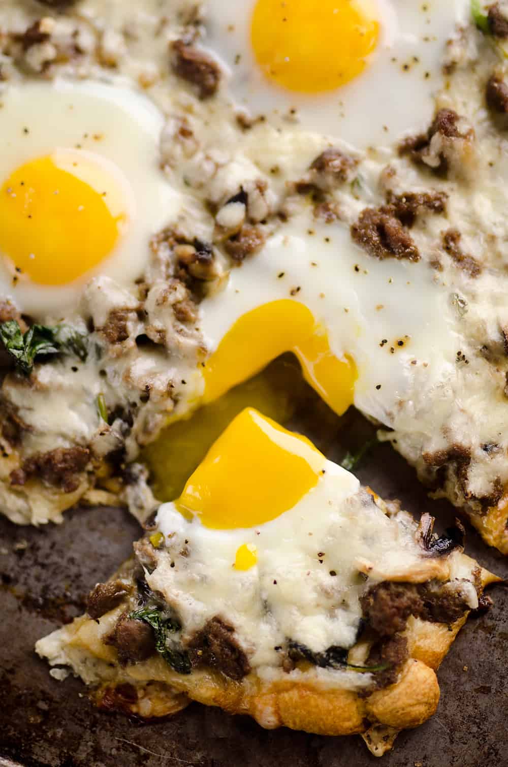 Extreme close up of turkey sausage breakfast pizza with a piece cut out showing a runny yolk.