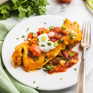 A keto breakfast enchilada topped with sour cream and salsa on a white plate.