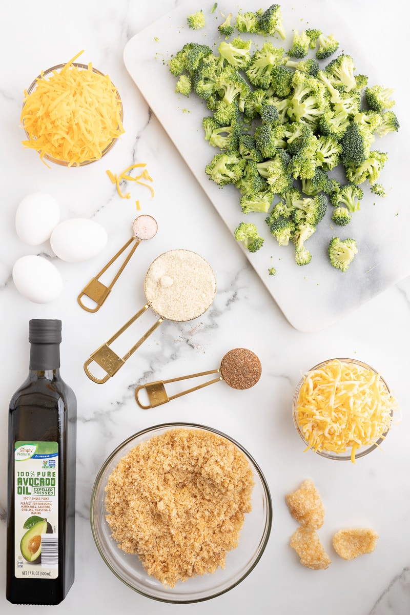 Overhead view of the ingredients needed to make keto broccoli cheese balls on a white marble counter.