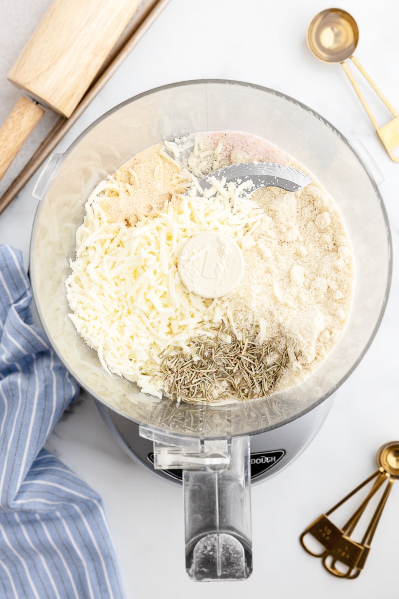 Almond flour, shredded cheese, rosemary, garlic powder, and salt in the bowl of a food processor.