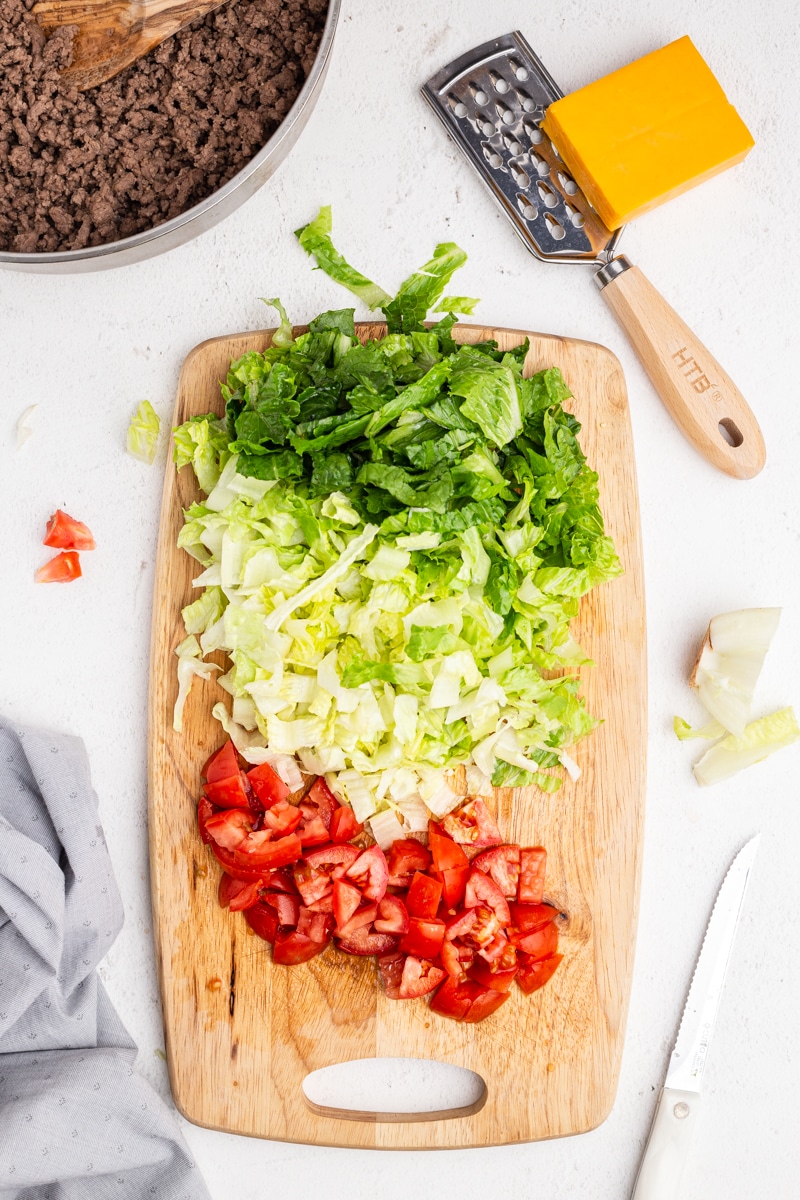 A small wooden cutting board with chopped tomato and Romaine lettuce on it.