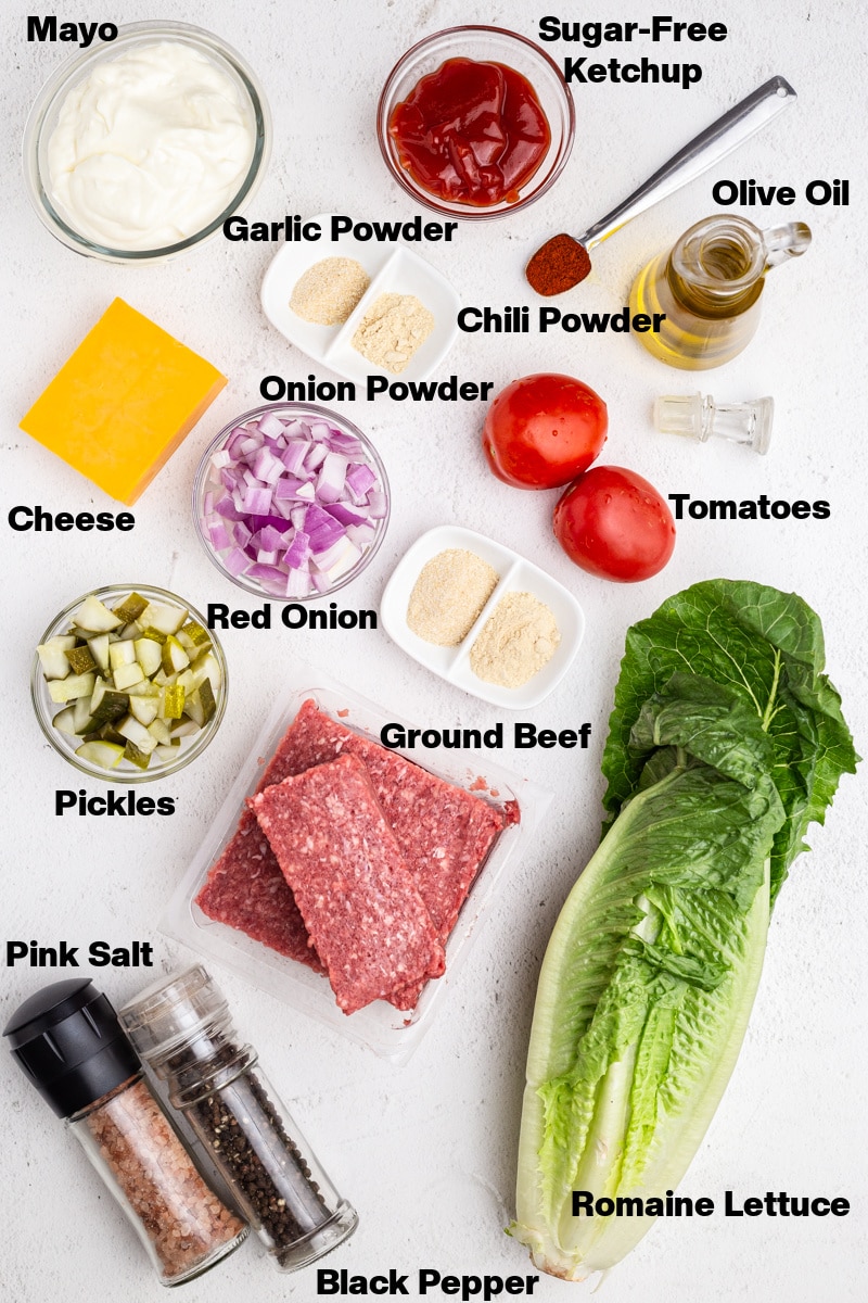 Overhead view of the ingredients needed to make Big Mac Salad in a Jar on a white marble counter.