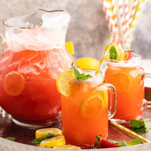 Image shows a glass pitcher full of Sugar-Free Strawberry Lemonade on a silver tray with 2 glass mugs full of the lemonade next to the pitcher.