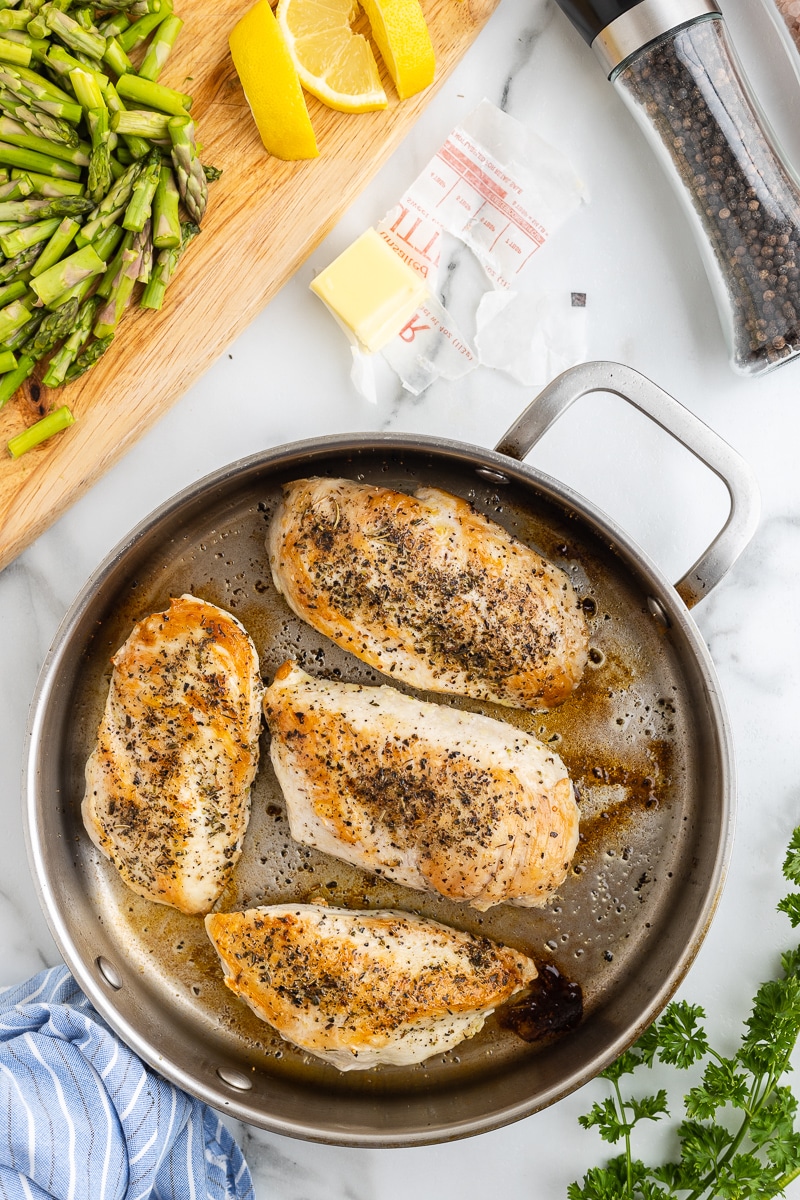 Seasoned chicken breasts seared in a large skillet on a white marble counter.