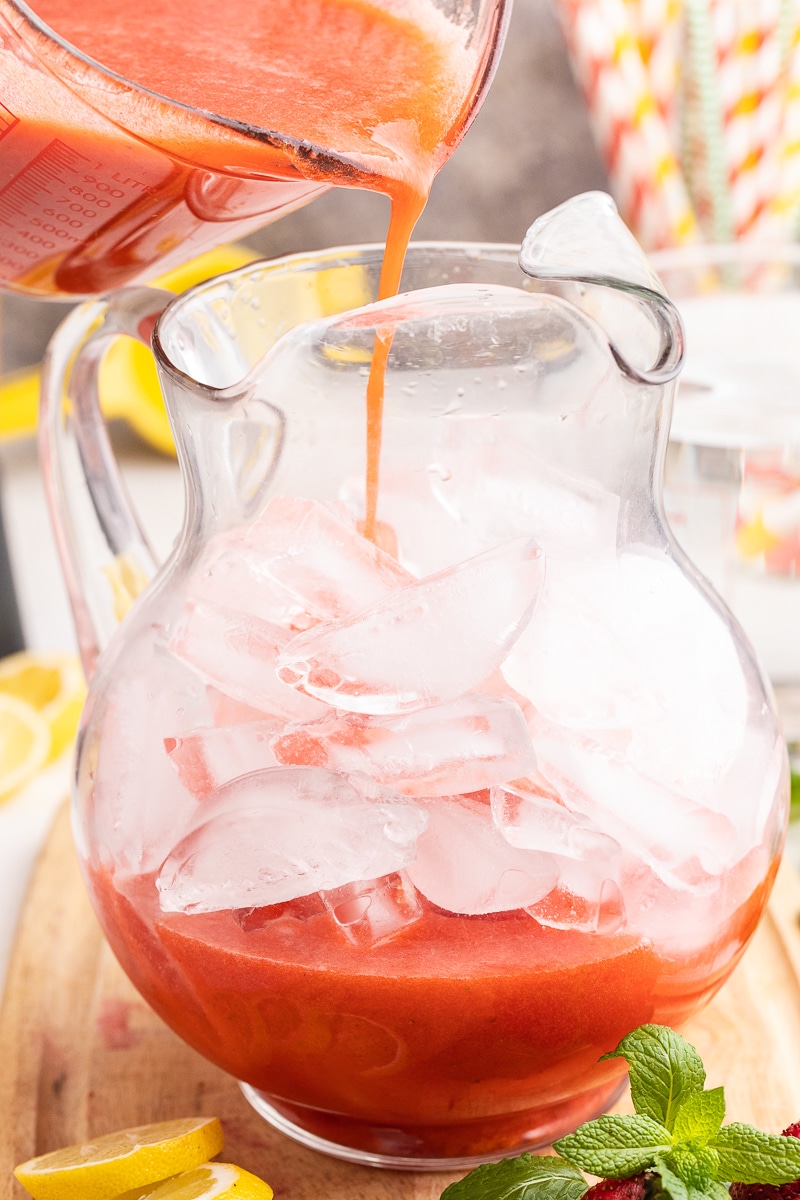 The image shows Sugar-Free Strawberry Lemonade being poured over ice into a beautiful glass pitcher.