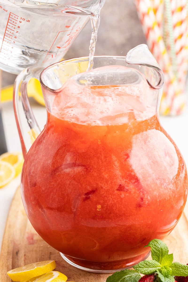 This image shows someone adding water to the Sugar-Free Strawberry Lemonade in a large glass pitcher.
