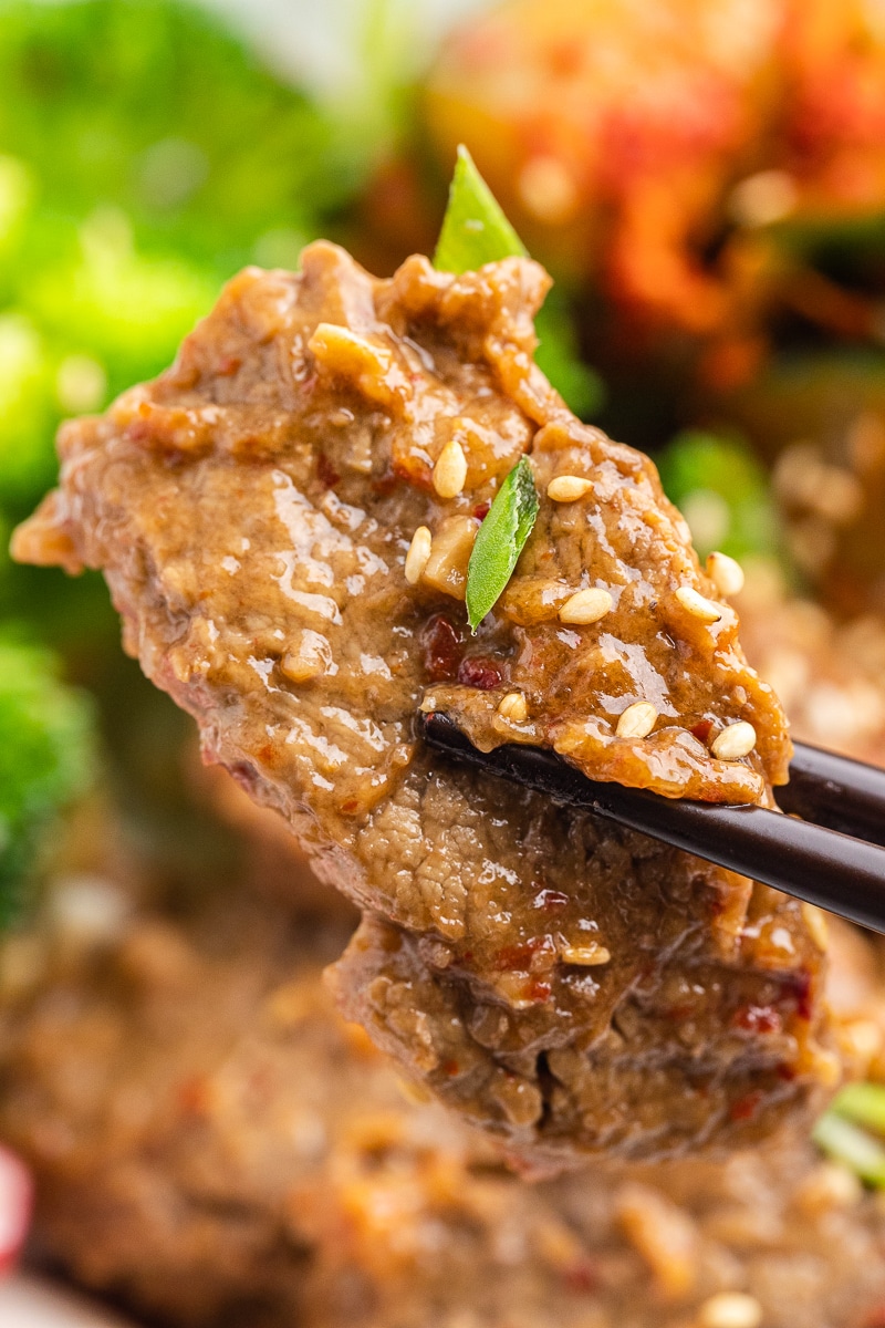 Closeup view of a delectable piece of Korean beef held delicately with chopsticks. The succulent beef is generously coated with the rich and flavorful sauce, and the glistening toasted sesame seeds add a delightful touch. The combination of savory flavors and enticing textures promises a truly satisfying experience in every bite of this Keto Korean Beef Bowl.