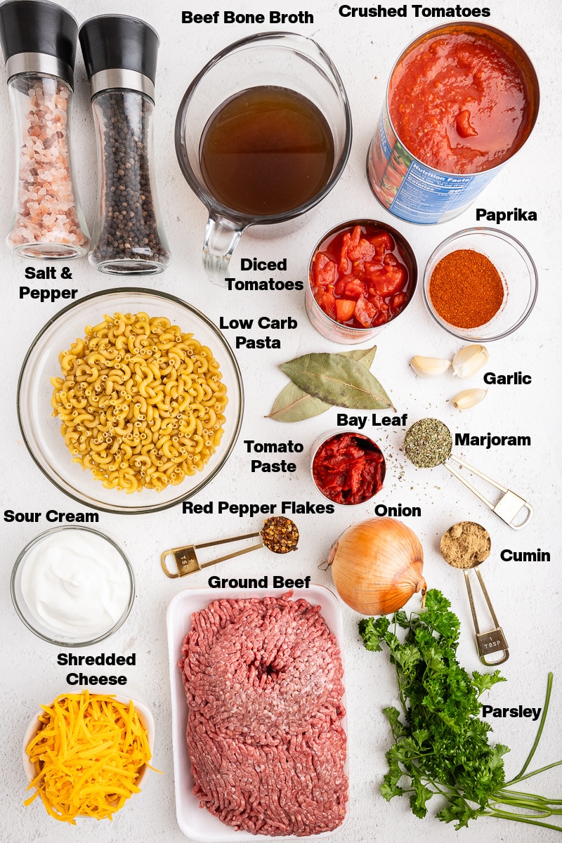 Overhead view of all of the ingredients needed to make Keto Goulash (American Chop Suey) on a white counter.