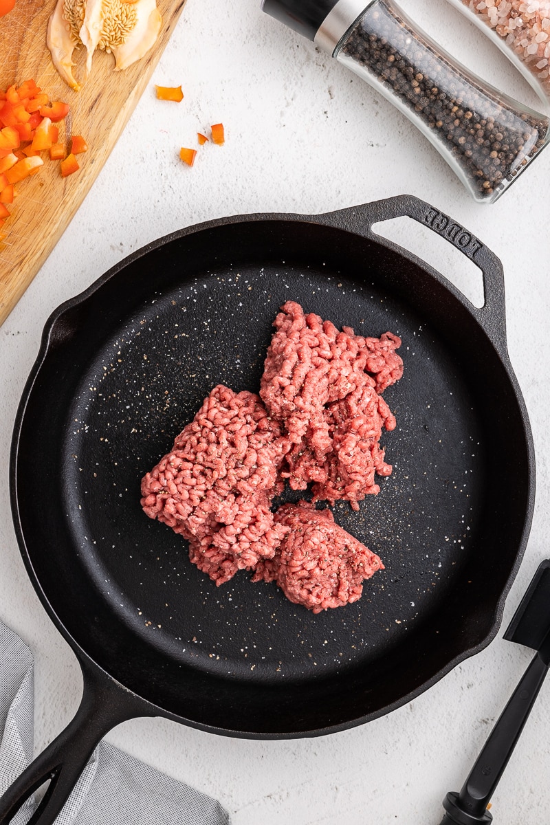 Overhead view of a cast iron skillet with ground beef cooking. Keto Sloppy Joes Recipe - Step 1: Preparing the flavorful base with seasoned ground beef in a skillet. Perfect low-carb comfort food for a delightful sloppy joe experience.