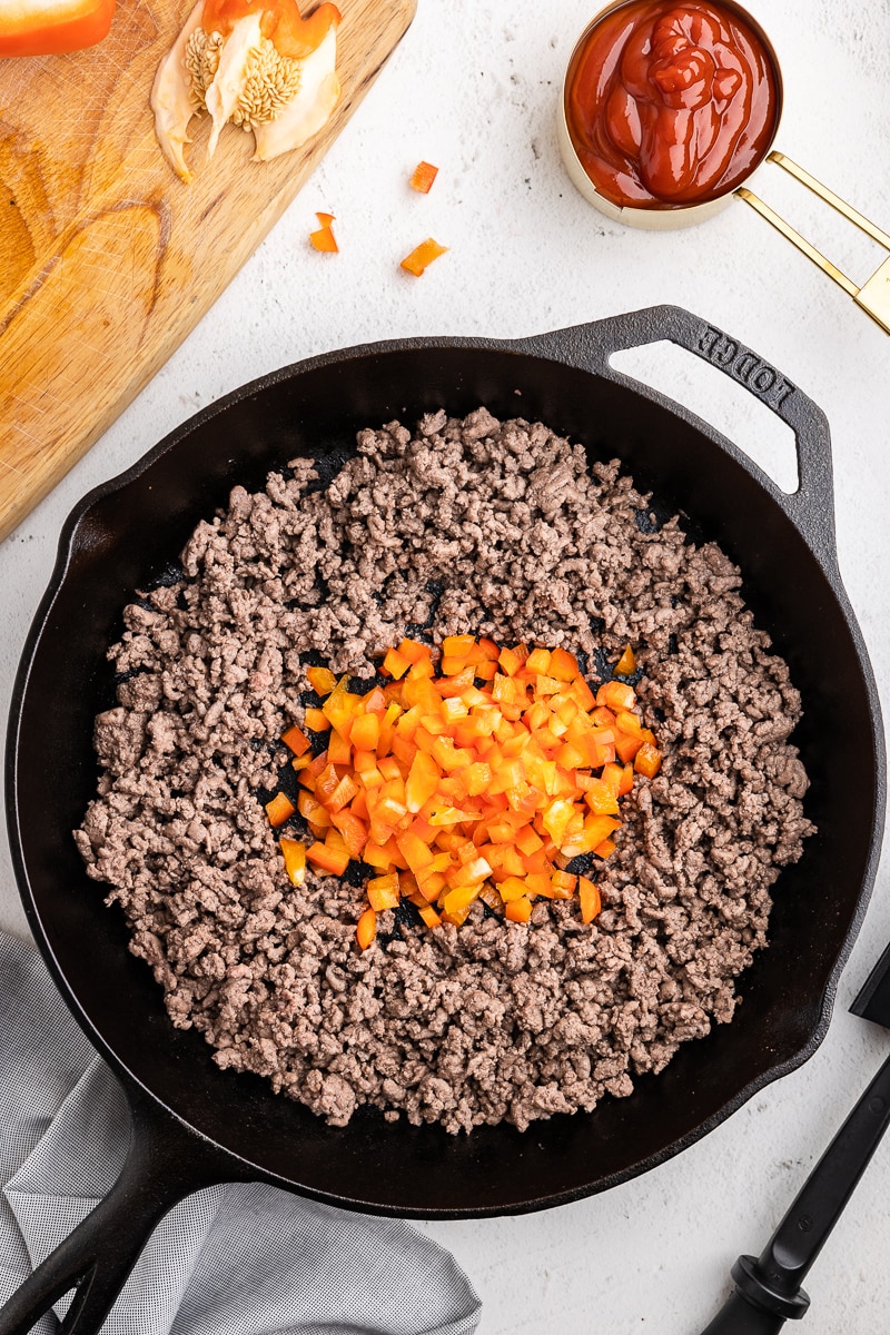 Step 2 of Keto Sloppy Joes Recipe - Browned ground beef with diced orange bell pepper placed in the center of the skillet. Cooking down the peppers for a deliciously flavorful and low-carb sloppy joe filling.