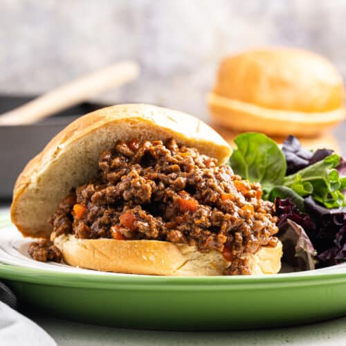 An extreme close-up of the mouthwatering keto sloppy joe mixture cascading over the bottom bun with the top bun perched on top. The delightful meal is showcased on a white plate, creating an enticing and appetizing image.