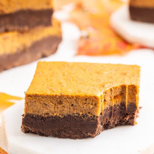 Close up of a keto pumpkin pie brownie with a bite taken out of it on a white plate with more brownies in the background.
