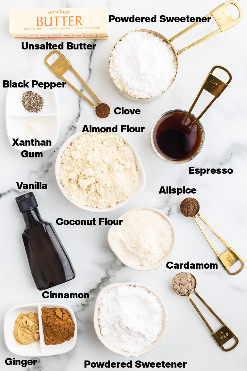 Overhead view of the ingredients needed to make keto chai sugar cookies on a white marble counter. Ingredients are labeled.