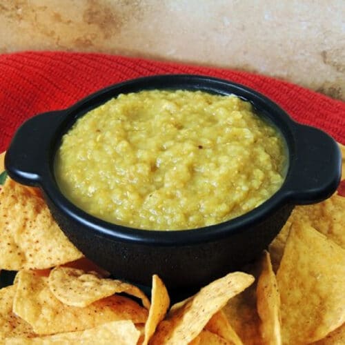 Close up of a black bowl full of roasted tomatillo salsa on a plate with keto tortilla chips.