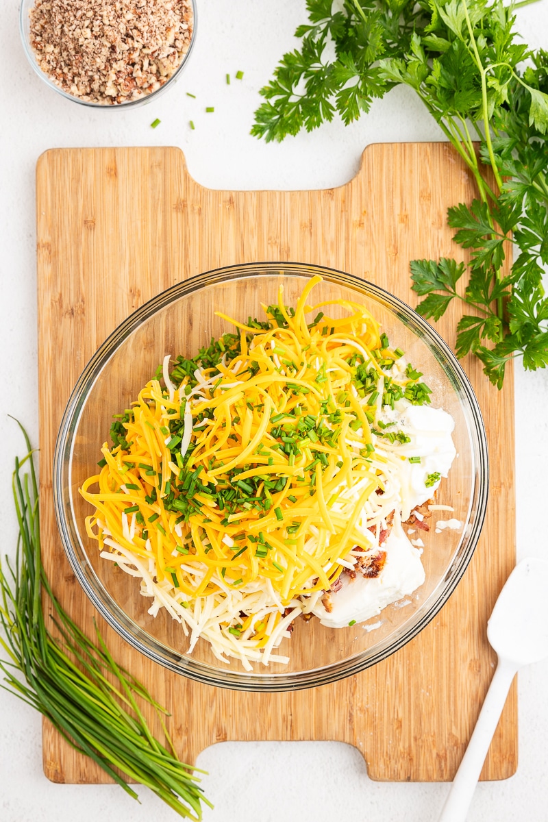 Overhead view of all of the ingredients needed to make a bacon ranch cheese ball in a large glass mixing bowl.