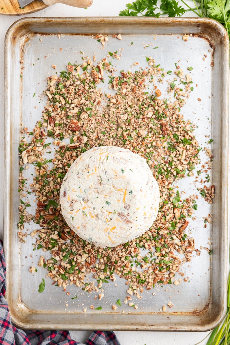 Rolling the cheeseball in chopped pecans and fresh parsley on a baking sheet.