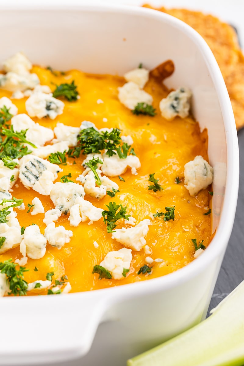 Buffalo Chicken Dip aka Chicken Crack in a white casserole dish topped with blue cheese crumbles and fresh chopped parsley.