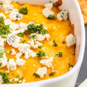 Buffalo Chicken Dip aka Chicken Crack in a white casserole dish topped with blue cheese crumbles and frech chopped parsley.