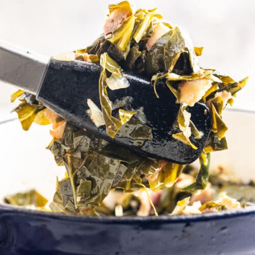 Closeup of a large blue Dutch oven full of Southern-Style Collard Greens with Bacon with tongs holding a serving above the pot.