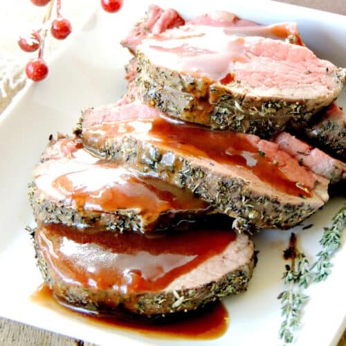 A close up of 4 slices of herb crusted beef tenderloin on a white serving tray topped with a cranberry port wine sauce.