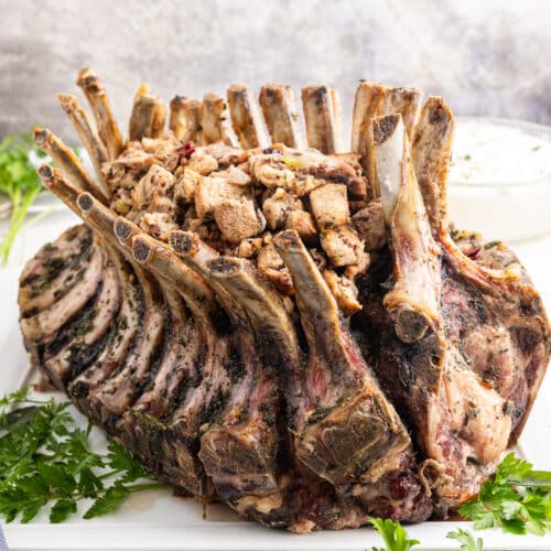 A pork crown roast on a white platter filled with keto cranberry pecan stuffing.