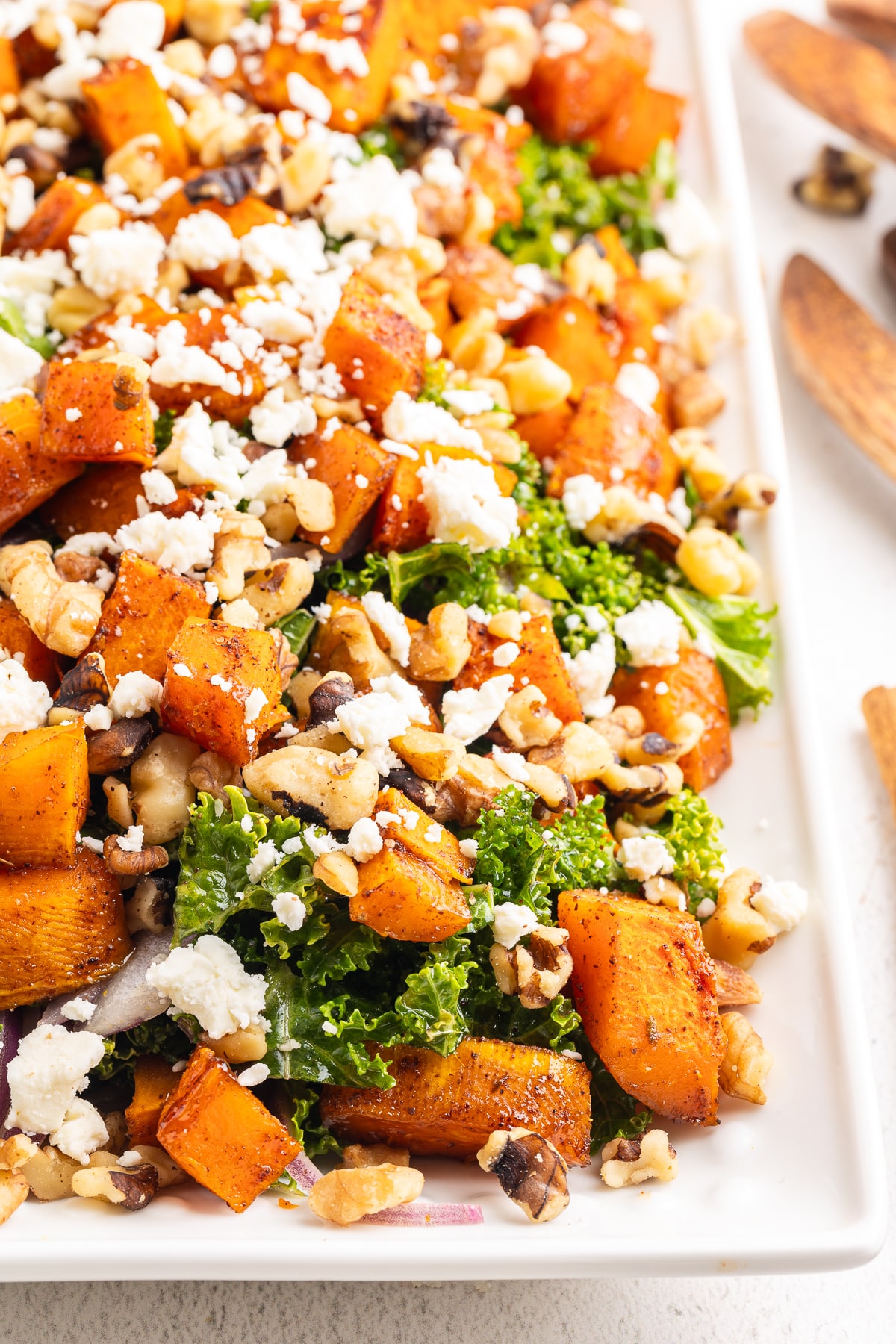 A closeup of a white serving tray full of Roasted Butternut Squash and Kale Salad.