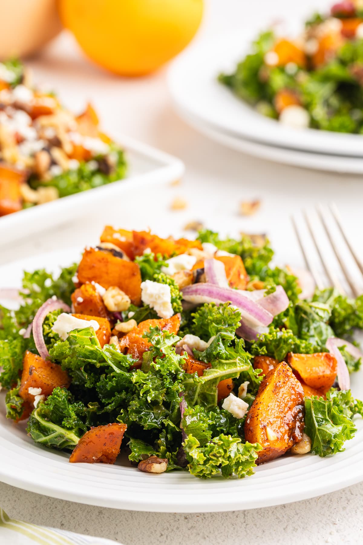 Roasted Butternut Squash and Kale Salad on a white plate with a serving tray with the remaining salad in the background.