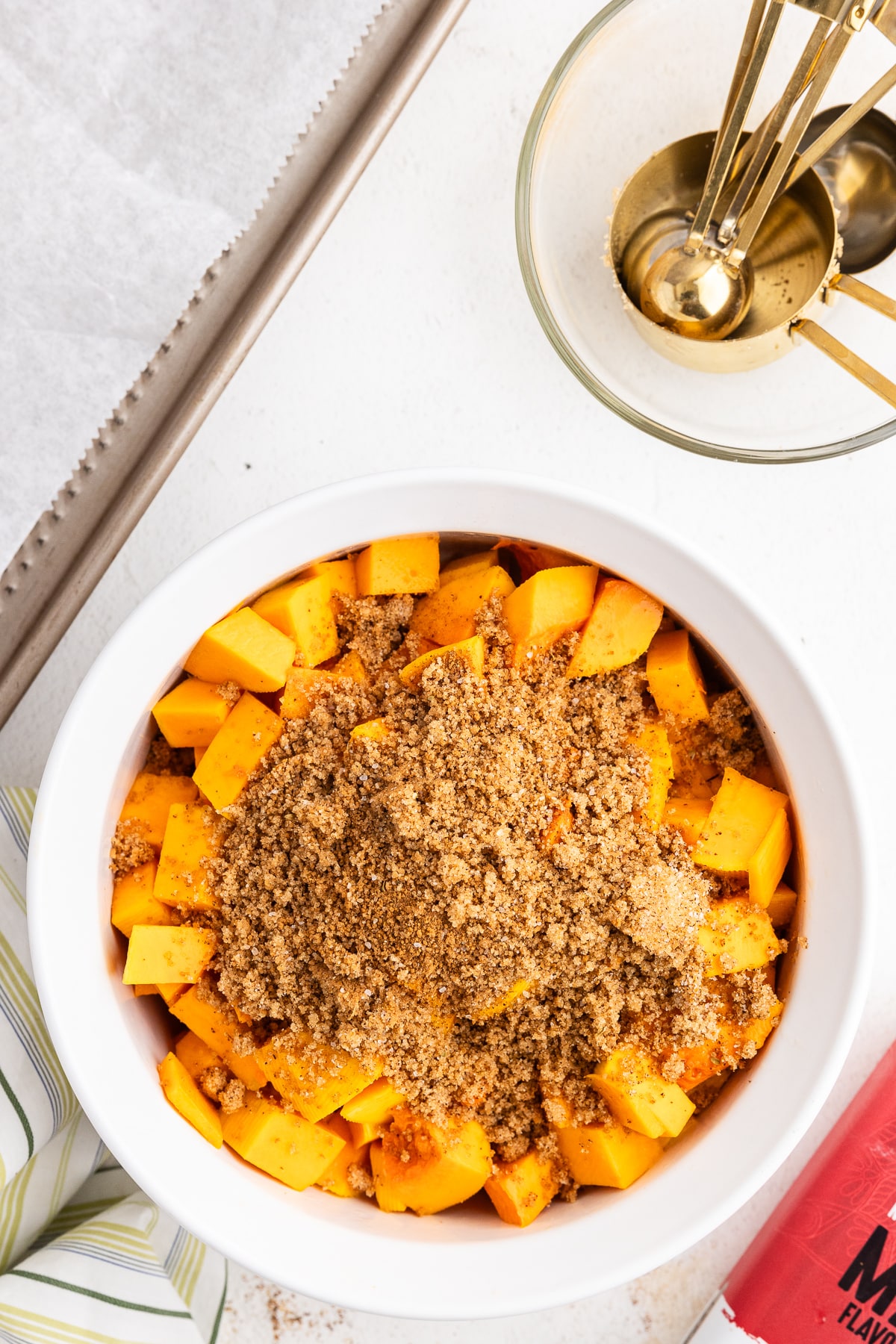 Overhead view of a white bowl full of butternut squash cubes and a keto brown sugar spice mixture.